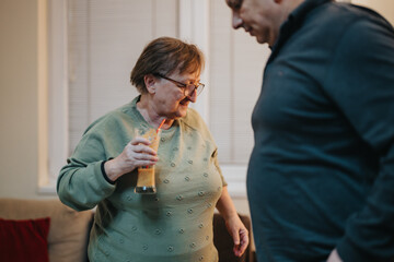 A senior woman smiles warmly while holding a beverage, engaging in a cheerful interaction. The cozy...