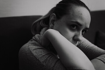 The image captures a woman resting her chin on her arm while sitting on a couch surrounded by a...