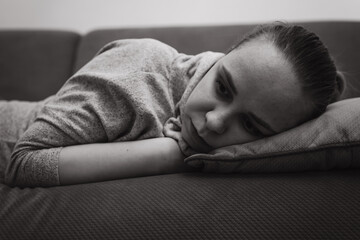 A young woman relaxes on a couch resting her head on a pillow while lost in thought The room has a...