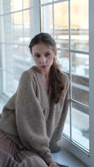 Beautiful young girl posing for the camera while sitting near a large window