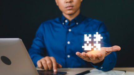 A businessman holds glowing puzzle pieces in his hand, symbolizing strategy and problemsolving with a laptop nearby
