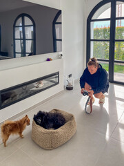 Midlife woman capturing moments with her camera, kneeling beside a cozy pet bed, surrounded by two...