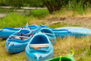 A group of vibrant blue kayaks can be seen peacefully resting on the grass beside a flowing river,...