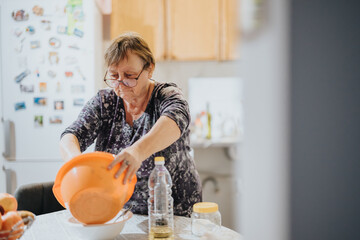 An elderly woman engaged in food preparation, carefully handling ingredients in a home setting. The...
