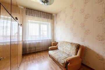 cozy room features floral wallpaper, a patterned sofa, and a window with sheer curtains. A wooden...
