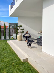 Woman working remotely on a laptop while sitting on a patio, surrounded by greenery and modern...