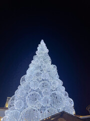 Illuminated Christmas tree adorned with sparkling lights and decorative spheres, towering against a...