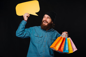 A cheerful man is joyfully holding colorful shopping bags and has a speech bubble in a creative,...