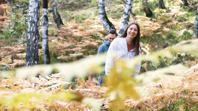 Married couple relaxing in nature during a walk in the autumn forest. Woman and man in love walking through tall yellow grass, in fern leaves - Powered by Adobe