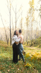 Fototapeta premium Married couple relaxing in nature during a walk in the autumn forest. Woman and man in love walking through tall yellow grass, in fern leaves