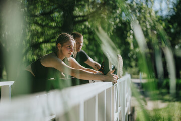 Couple practicing stretching exercises together on a bridge surrounded by lush greenery. The...