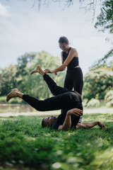A pair of individuals engaged in acrobatic exercises on the grass within a park setting.