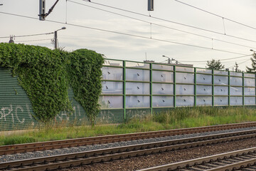 Urban railway tracks feature a durable sound barrier, blending natural green ivy and transparent...
