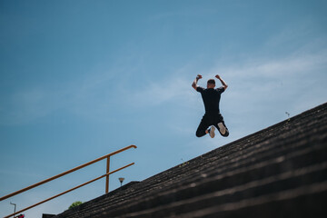 A person performs a jump on large steps in an outdoor park with bright sunlight and clear skies,...