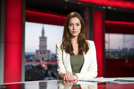 A poised female news anchor sits confidently at her desk in a modern news studio, preparing for the evening broadcast. The sleek lighting and professional setup highlight authority, 