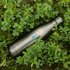 Stylish insulated bottle nestled among lush green clovers in a peaceful nature setting during midday