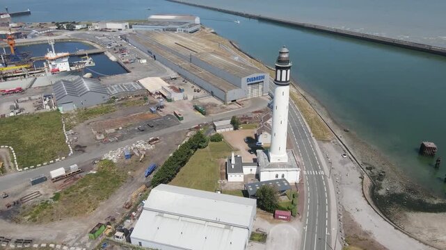 Aerial view of the stark white Dunkirk Lighthouse standing tall against the blue water and the city backdrop, Dunkirk, Hauts-de-France, France.