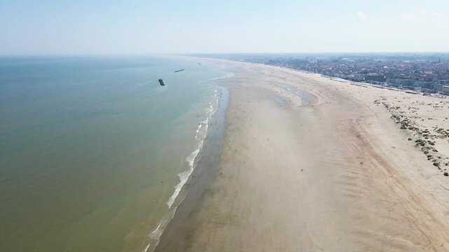 Aerial view of the beach where the gentle waves meet the sandy shore, speckled with people enjoying the sun, Dunkirk, Hauts-de-France, France.