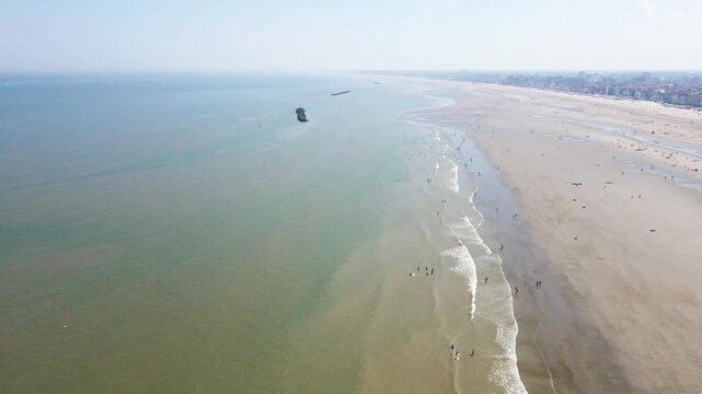 Aerial view of the beach with people along the shoreline and an offshore structure contrasting against the sea, Dunkirk, Hauts-de-France, France.