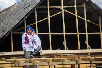 two builders reconstruct a wooden house, repairing a wall and a pediment