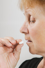 An elderly woman brings a pill to her mouth.