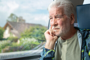 Serious bearded old senior man sitting on train, savoring time spent on the journey, looking out of window, having time to admire the passing landscape