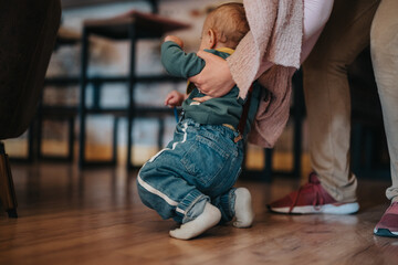 A baby in comfortable clothing being helped by an attentive adult while exploring crawling motions...