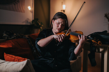 A woman plays the violin with emotion and concentration while seated in a comfortable, warmly lit...