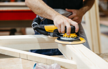 Worker sanding wooden beam with electric sander in aluminum workshop