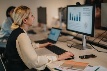 A businesswoman focuses on data analysis while working at a computer in a collaborative office setting, reflecting teamwork and professional growth.