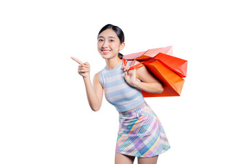 A happy young Asian woman with shopping bags, pointing to the side to show an exciting sale or...