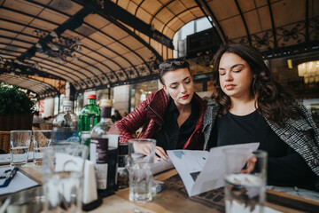 Two professional women engage in a discussion over documents at an outdoor venue. The setting is...