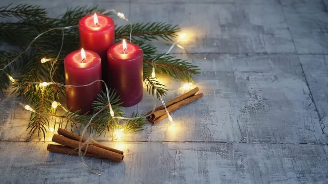 A beautiful Christmas or Advent centerpiece with three burning red candles, fresh pine branches, cinnamon sticks, and fairy lights on a rustic wooden table.