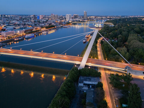 Aerial view of the illuminated Most SNP bridge stretching across the tranquil Danube River, with the cityscape shimmering in the twilight, Bratislava, Bratislava Region, Slovakia.