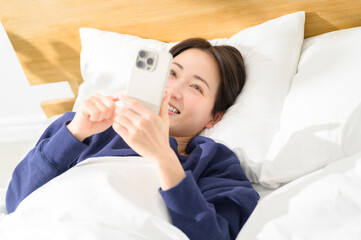 A Japanese woman operating her smartphone on her back in bed