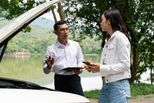 Car Troubleshooting. Mechanic explaining vehicle issues to a woman by the lakeside.