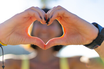 Smiling girl making love sign at sunset. Portrait of young smiling charming woman showing heart...