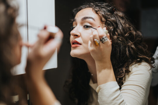 A young woman is seen applying makeup in front of a mirror, demonstrating concentration and engagement in her personal beauty routine, with a natural and home-based setting.