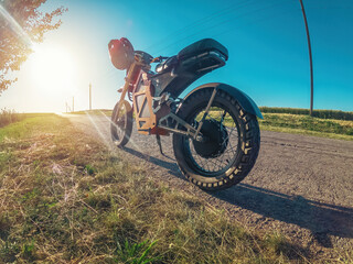 Electric motorcycle on side of road, standing near tree. Moped modern personal transport. Sunset.