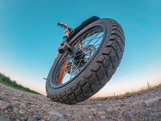 Creative photo of zoomed electric motorcycle wheel, low angle view. Arcing horizon with blue sky.