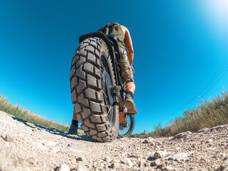 Creative photo of zoomed electric motorcycle with biker, low angle view. Arcing horizon, blue sky.