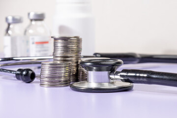 Stacks of coins alongside a stethoscope rest on a desk, symbolizing the financial burden and budgeting associated with healthcare, insurance, and medical expenses.

