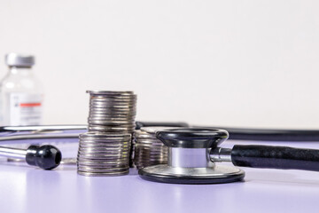 Stacks of coins alongside a stethoscope rest on a desk, symbolizing the financial burden and...