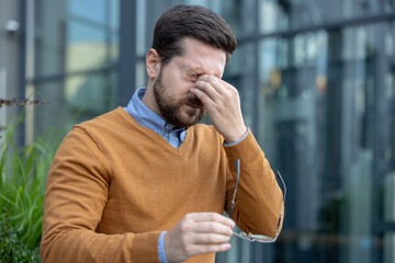 Close-up photo of a young male businessman sitting outside a work building on the street, holding a...
