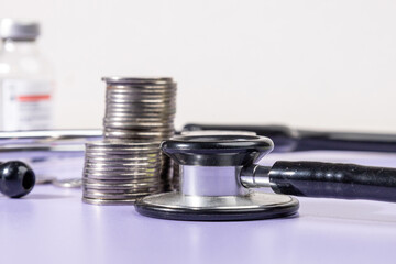 Stacks of coins alongside a stethoscope rest on a desk, symbolizing the financial burden and...
