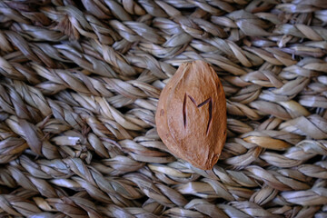 A single apricot pit with a carved rune rests on a textured straw mat. The minimalist composition...