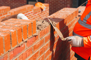 Industrial bricklayer laying bricks and concrete blocks on cement mix mortar on construction site