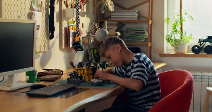 A boy enthusiastically builds a robot from a construction kit while sitting at a table at home