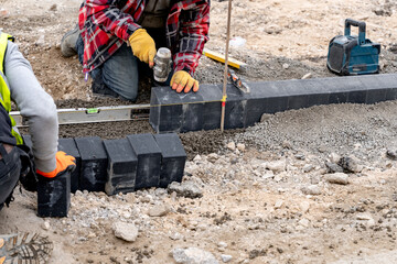 Footpath construction as workers laying block paving bricks and leveling concrete on construction...
