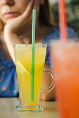 Two colorful beverages sit on a table as one person reflects quietly in a cafe setting The atmosphere is relaxed with natural light illuminating the space